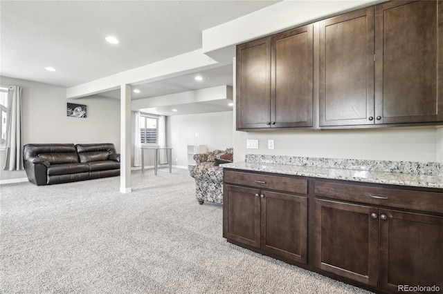 kitchen with light colored carpet, light stone counters, and dark brown cabinetry