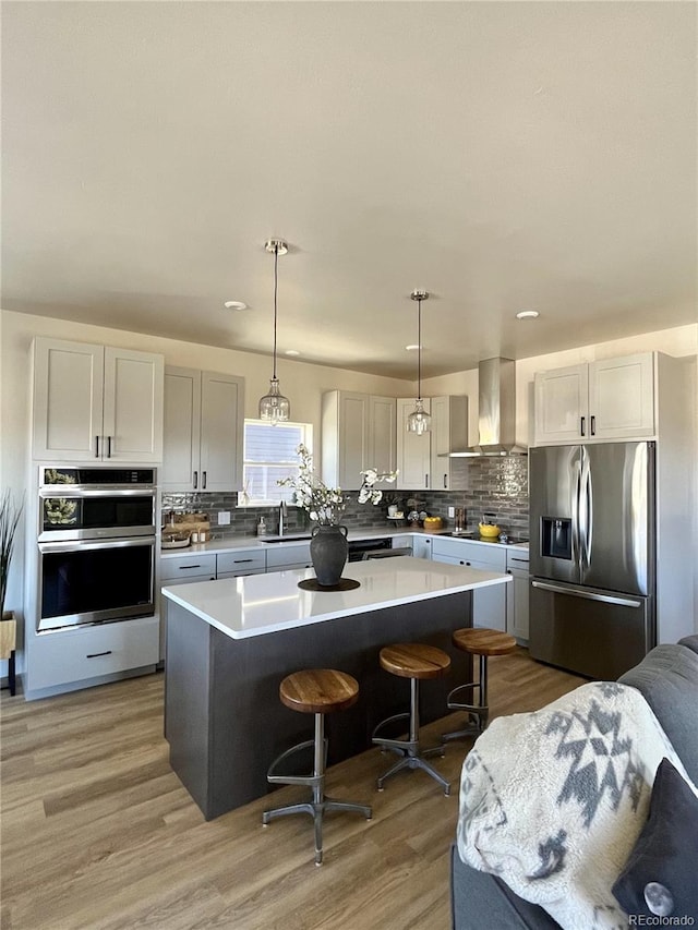 kitchen featuring appliances with stainless steel finishes, a center island, wall chimney range hood, hanging light fixtures, and a breakfast bar area