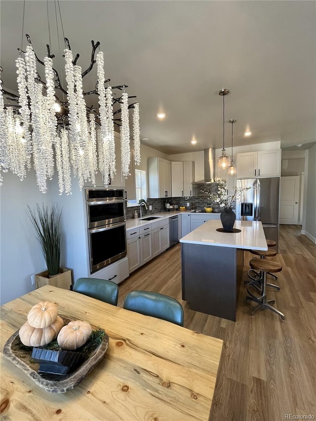 kitchen featuring a center island, appliances with stainless steel finishes, hanging light fixtures, backsplash, and wall chimney exhaust hood