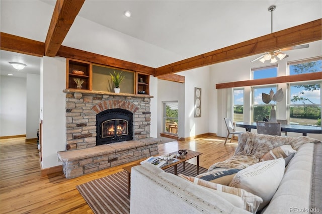 living room with ceiling fan, a stone fireplace, beamed ceiling, and light hardwood / wood-style flooring