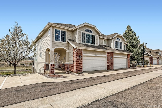 traditional-style home featuring brick siding, a garage, concrete driveway, and a shingled roof