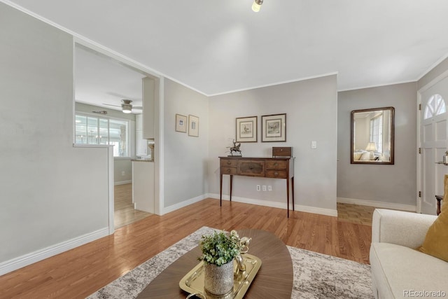 living room with a ceiling fan, baseboards, crown molding, and light wood finished floors