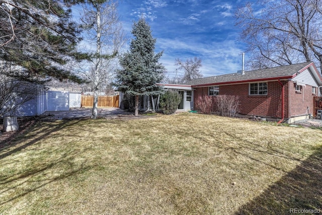 rear view of house featuring brick siding, a yard, and fence