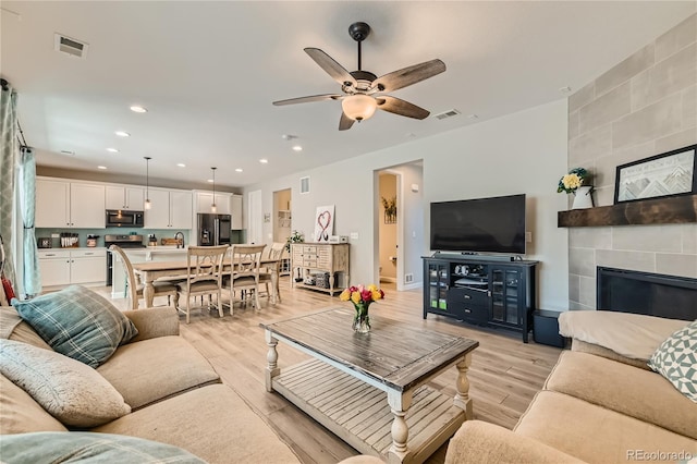 living room with a tile fireplace, light hardwood / wood-style floors, sink, and ceiling fan