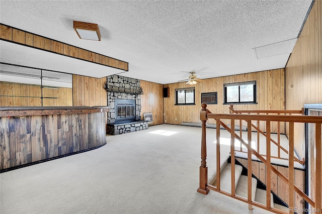 interior space with carpet flooring, ceiling fan, wood walls, a textured ceiling, and a fireplace