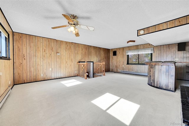 carpeted empty room with baseboard heating, ceiling fan, wooden walls, and a textured ceiling