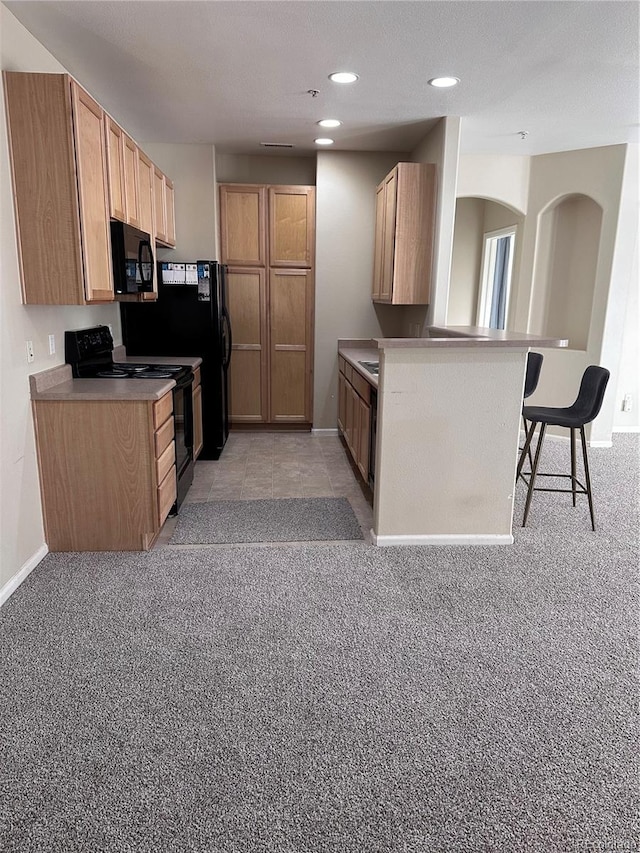 kitchen with light carpet, a breakfast bar, black appliances, kitchen peninsula, and light brown cabinets