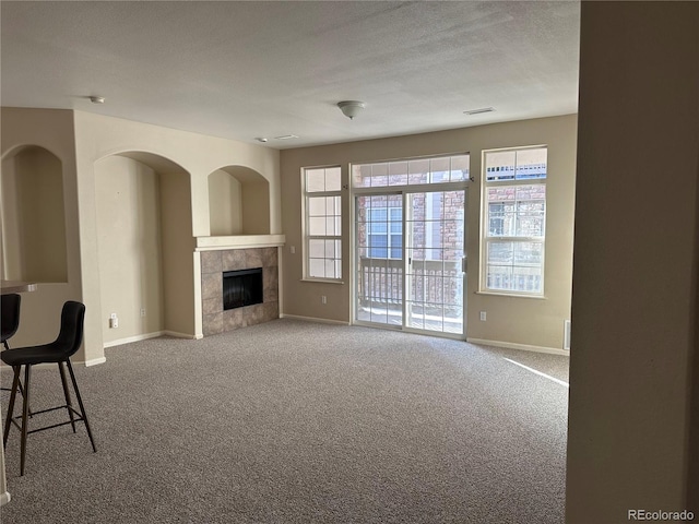 unfurnished living room with carpet, a textured ceiling, and a tile fireplace