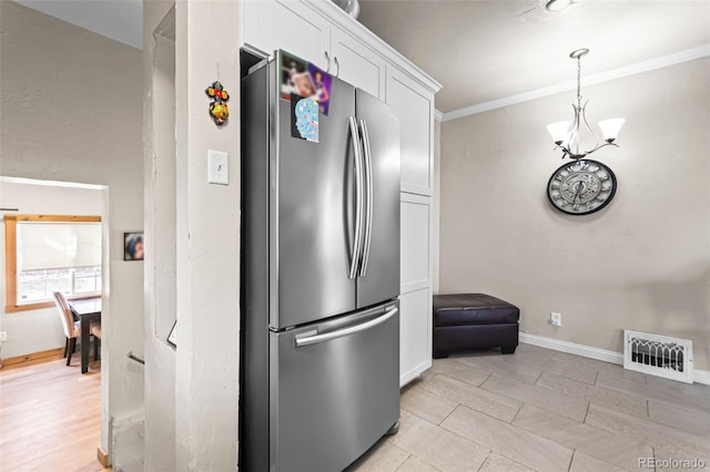 kitchen featuring white cabinetry, crown molding, an inviting chandelier, decorative light fixtures, and stainless steel refrigerator