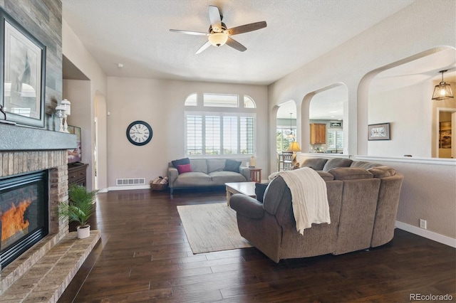 living room with ceiling fan, dark hardwood / wood-style flooring, a textured ceiling, and a brick fireplace