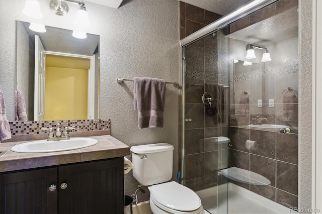 bathroom with vanity, tasteful backsplash, toilet, and a shower with shower door