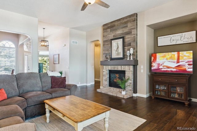 living room with a fireplace, ceiling fan, and dark wood-type flooring