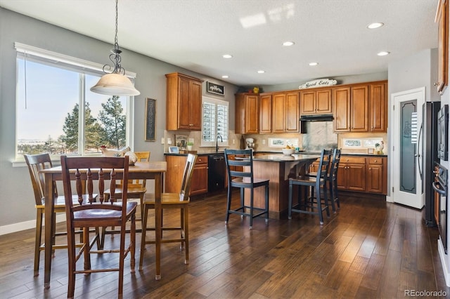 kitchen featuring dishwasher, a kitchen breakfast bar, hanging light fixtures, a kitchen island, and dark hardwood / wood-style flooring