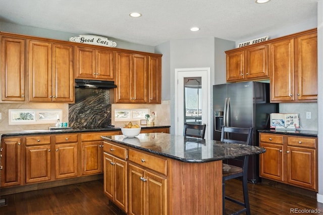 kitchen featuring a breakfast bar, a center island, dark stone counters, dark hardwood / wood-style floors, and stainless steel fridge