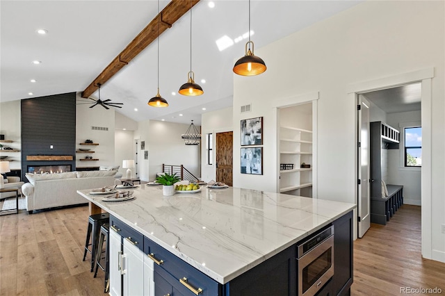 kitchen with beam ceiling, light hardwood / wood-style flooring, stainless steel microwave, and a large island