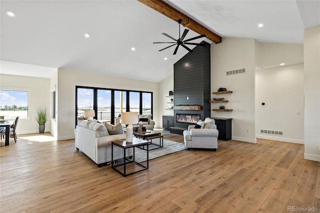 living room featuring a large fireplace, light hardwood / wood-style floors, beam ceiling, and high vaulted ceiling