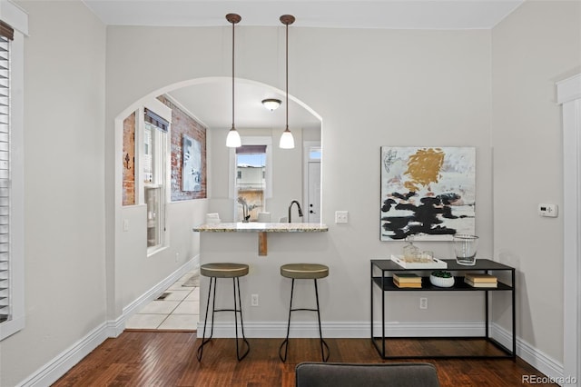 kitchen featuring dark wood-type flooring, decorative light fixtures, a kitchen breakfast bar, kitchen peninsula, and light stone countertops