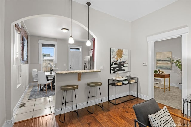 kitchen with dark hardwood / wood-style floors, a breakfast bar, stainless steel refrigerator, decorative light fixtures, and kitchen peninsula