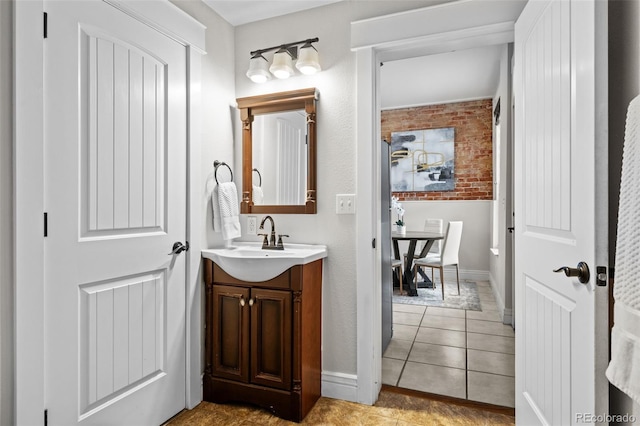 bathroom featuring tile patterned flooring, vanity, and brick wall