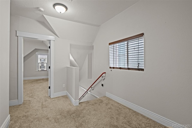 hall featuring lofted ceiling, light carpet, and a textured ceiling