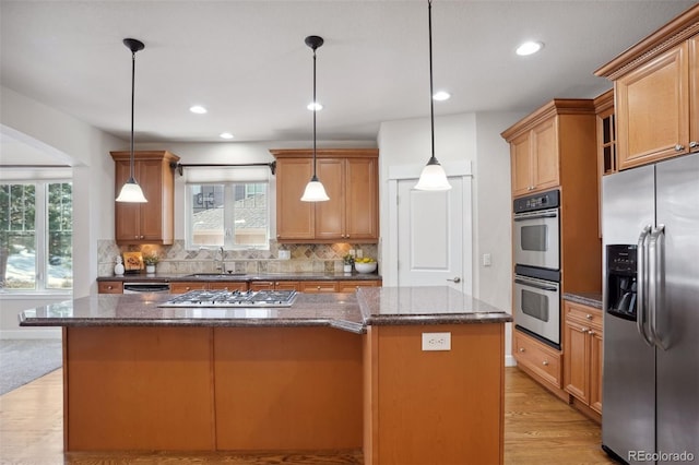 kitchen featuring stainless steel appliances, sink, decorative light fixtures, a center island, and light hardwood / wood-style floors