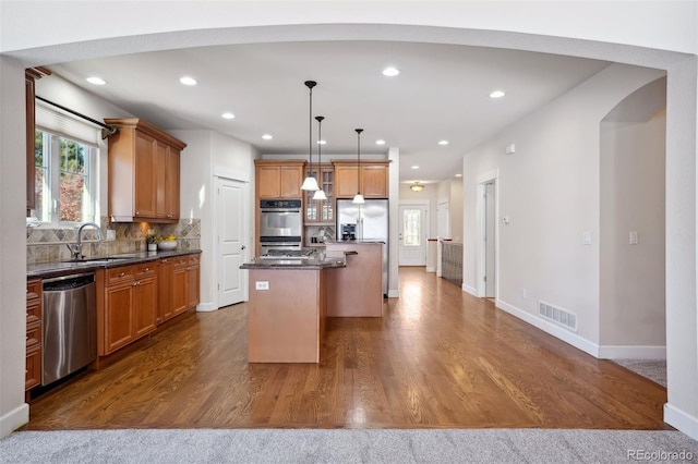 kitchen with sink, a center island, hanging light fixtures, hardwood / wood-style floors, and appliances with stainless steel finishes