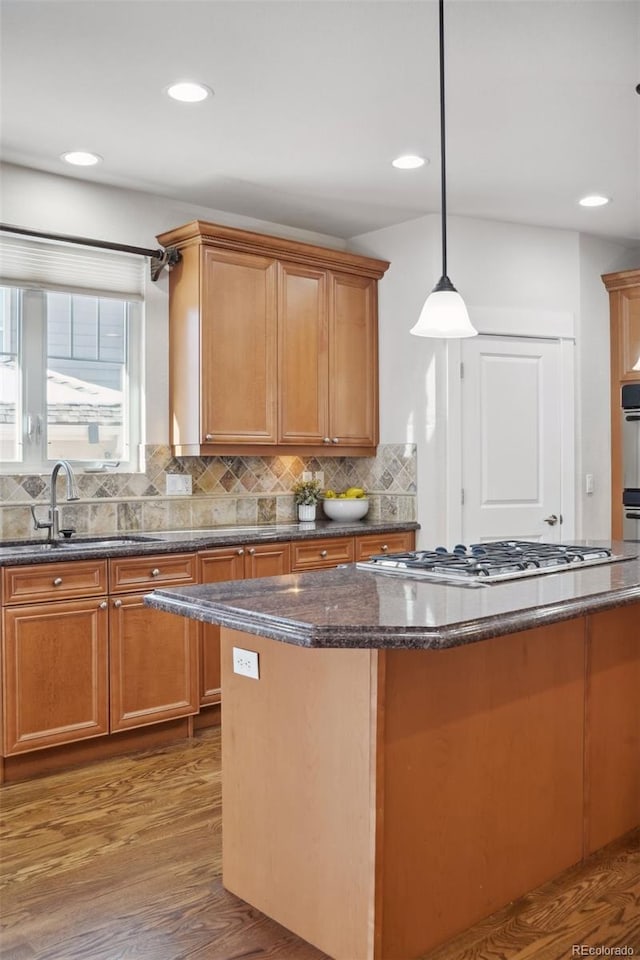 kitchen with decorative backsplash, appliances with stainless steel finishes, sink, wood-type flooring, and pendant lighting