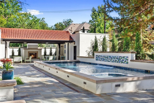 view of pool featuring pool water feature, a hot tub, an outdoor fireplace, and a patio