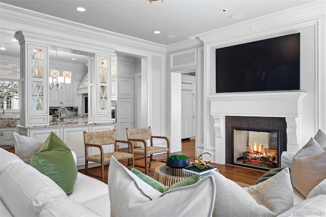 living room featuring a multi sided fireplace, crown molding, hardwood / wood-style floors, a chandelier, and sink