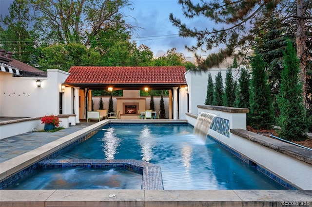 pool at dusk with a patio and an in ground hot tub