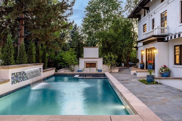 view of swimming pool with an outdoor fireplace, a patio area, and pool water feature