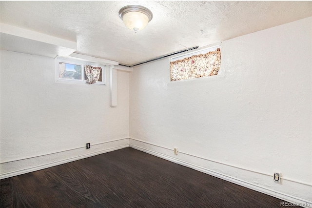 below grade area with dark wood finished floors, a textured ceiling, and baseboards