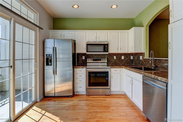 kitchen with appliances with stainless steel finishes, white cabinets, a sink, and backsplash