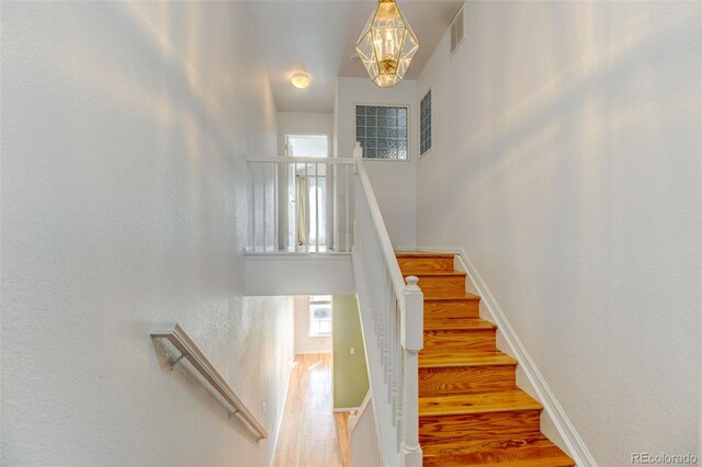 staircase featuring baseboards, visible vents, a towering ceiling, wood finished floors, and a chandelier