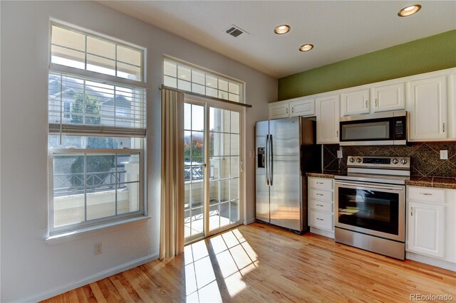 kitchen with white cabinets, dark countertops, light wood-style flooring, appliances with stainless steel finishes, and backsplash