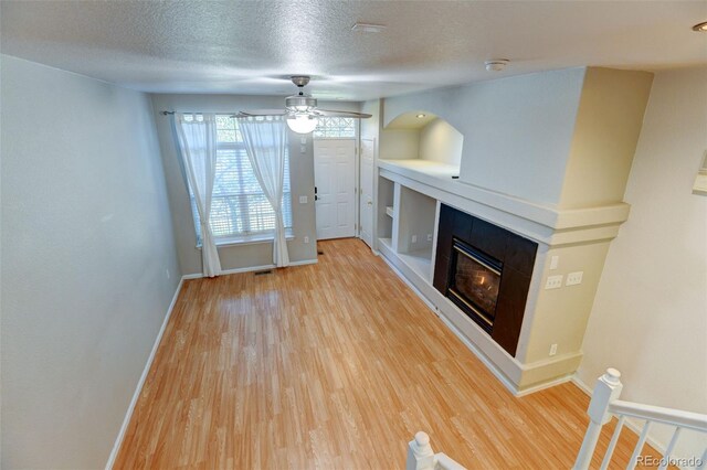 unfurnished living room featuring ceiling fan, a textured ceiling, wood finished floors, baseboards, and a glass covered fireplace