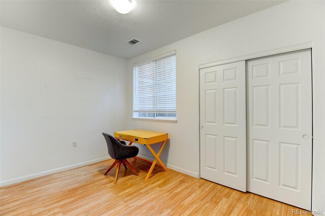 office area with a textured ceiling, wood finished floors, visible vents, and baseboards