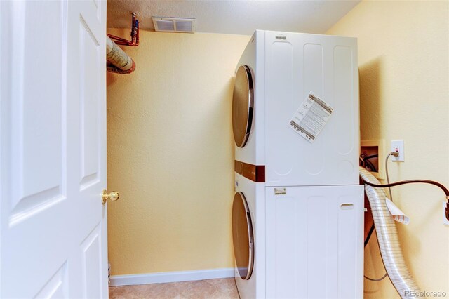 clothes washing area featuring laundry area, light tile patterned floors, baseboards, visible vents, and stacked washing maching and dryer