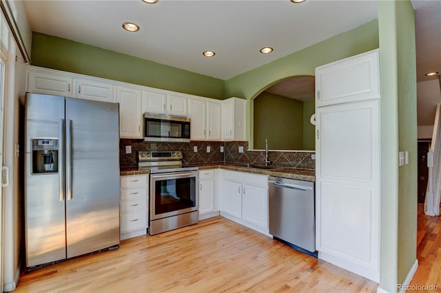 kitchen with tasteful backsplash, appliances with stainless steel finishes, light wood-style floors, white cabinetry, and a sink