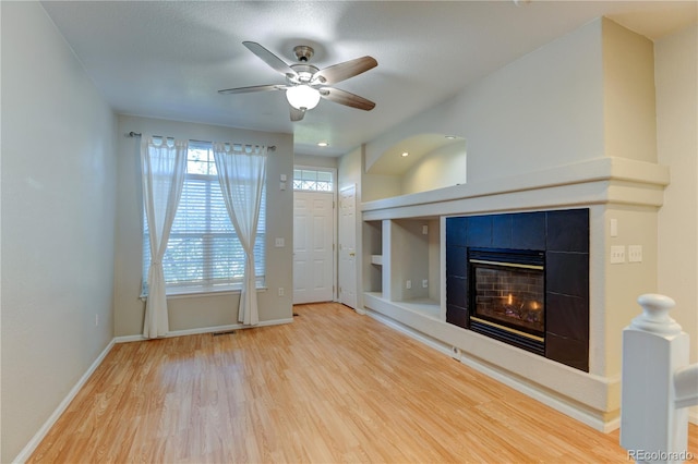 unfurnished living room featuring built in features, baseboards, a tiled fireplace, ceiling fan, and wood finished floors