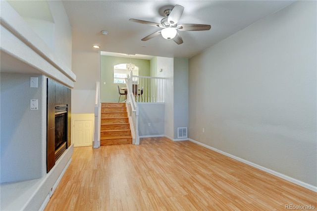 empty room with baseboards, visible vents, a tile fireplace, stairs, and light wood-type flooring