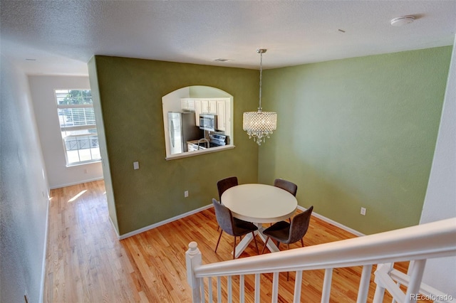 dining area featuring light wood finished floors, baseboards, a textured ceiling, and an inviting chandelier