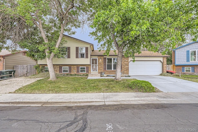 tri-level home with brick siding, an attached garage, a front lawn, fence, and driveway