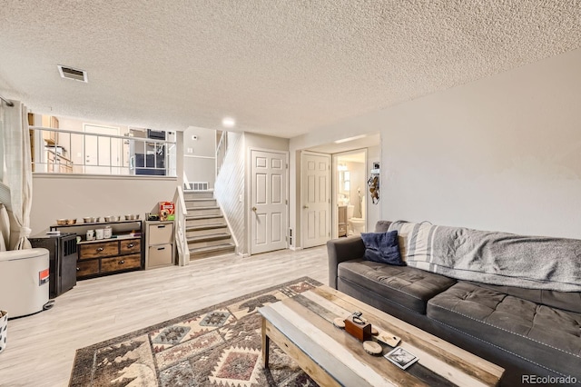 living room featuring visible vents, a textured ceiling, stairs, and wood finished floors