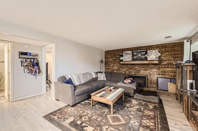 living room with visible vents, light wood-style flooring, a textured ceiling, a fireplace, and baseboards