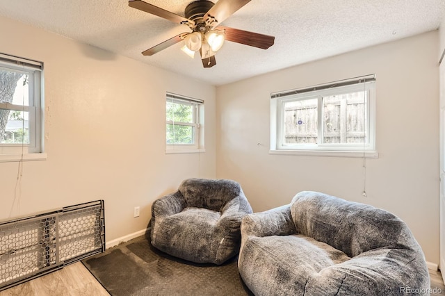 living area featuring baseboards, a textured ceiling, wood finished floors, and a ceiling fan