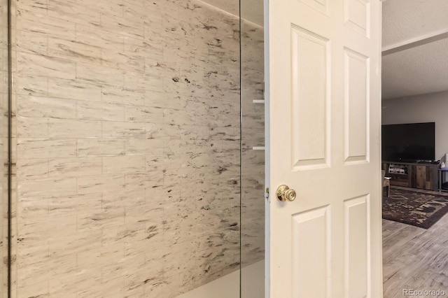 full bath with a textured ceiling, wood finished floors, and tiled shower