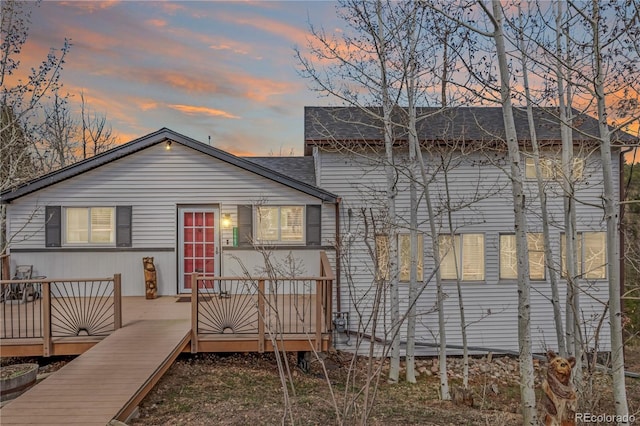 back of property at dusk with a wooden deck and a shingled roof