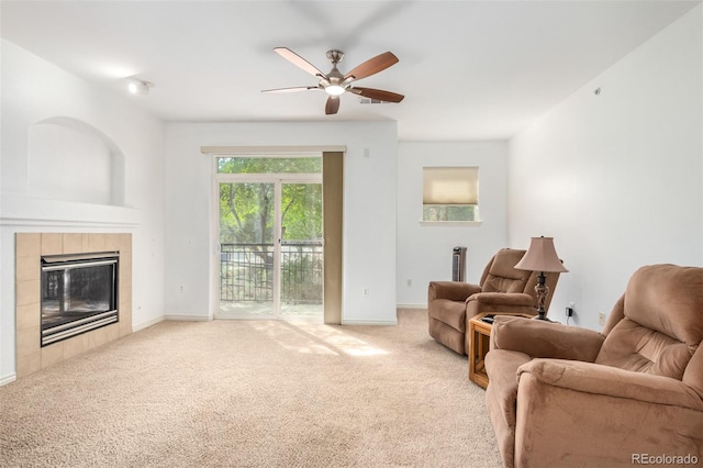 living room with a tiled fireplace, light colored carpet, and ceiling fan