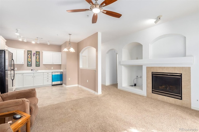 living room featuring light colored carpet, a tiled fireplace, ceiling fan with notable chandelier, and sink